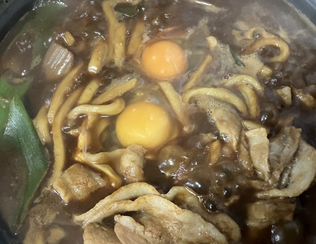 煮込んだ鍋焼きうどんに卵を入れた画像