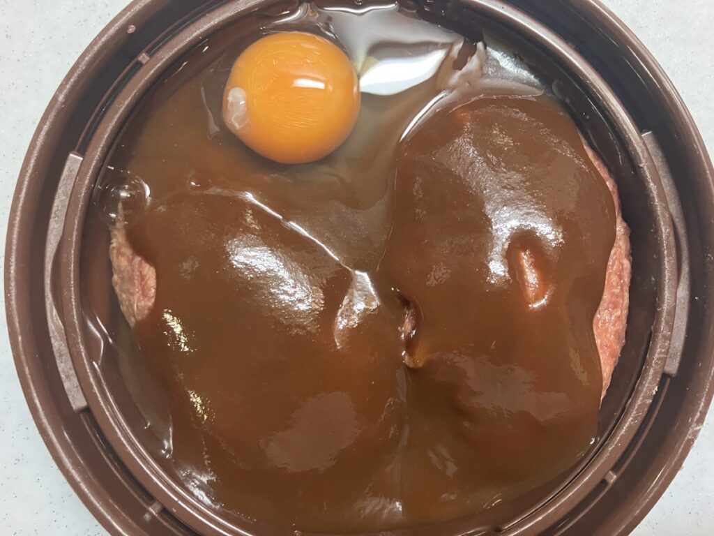 クッキングプレートにハンバーグのタネ、デミグラスソース、卵を入れた画像