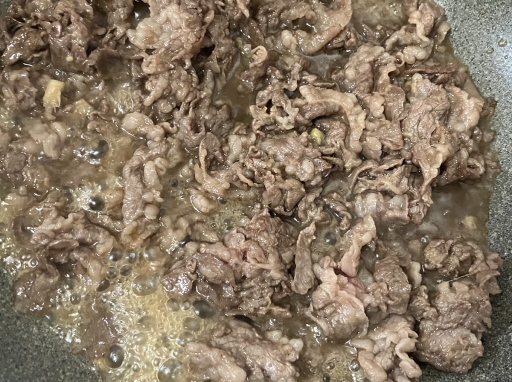 醤油、みりん、砂糖、酒を入れ煮立てながら肉と絡めている画像